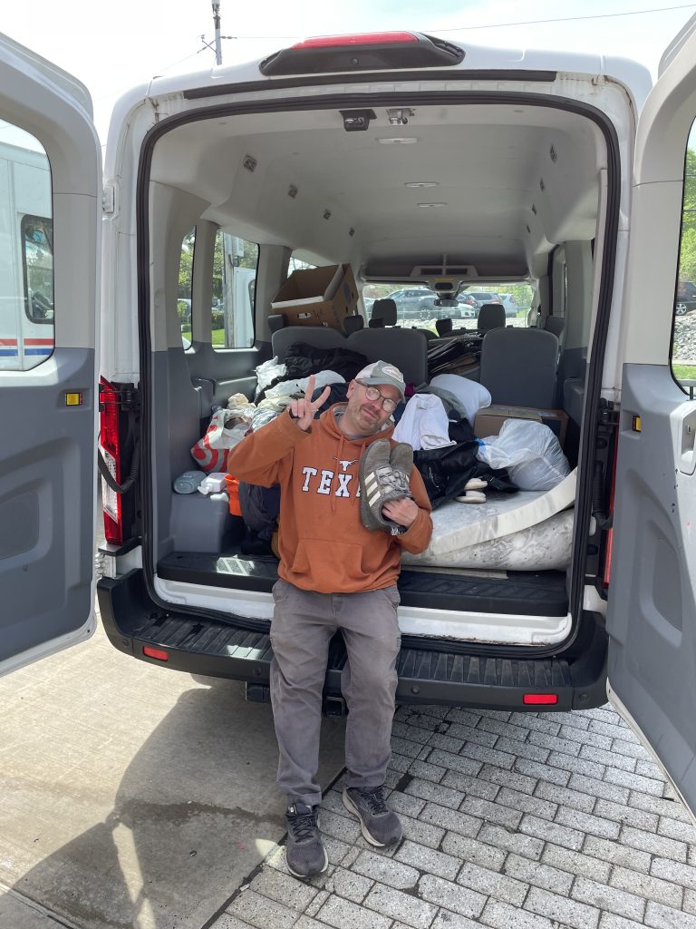 Individual from Catholic Charities poses in front of van full of donations.